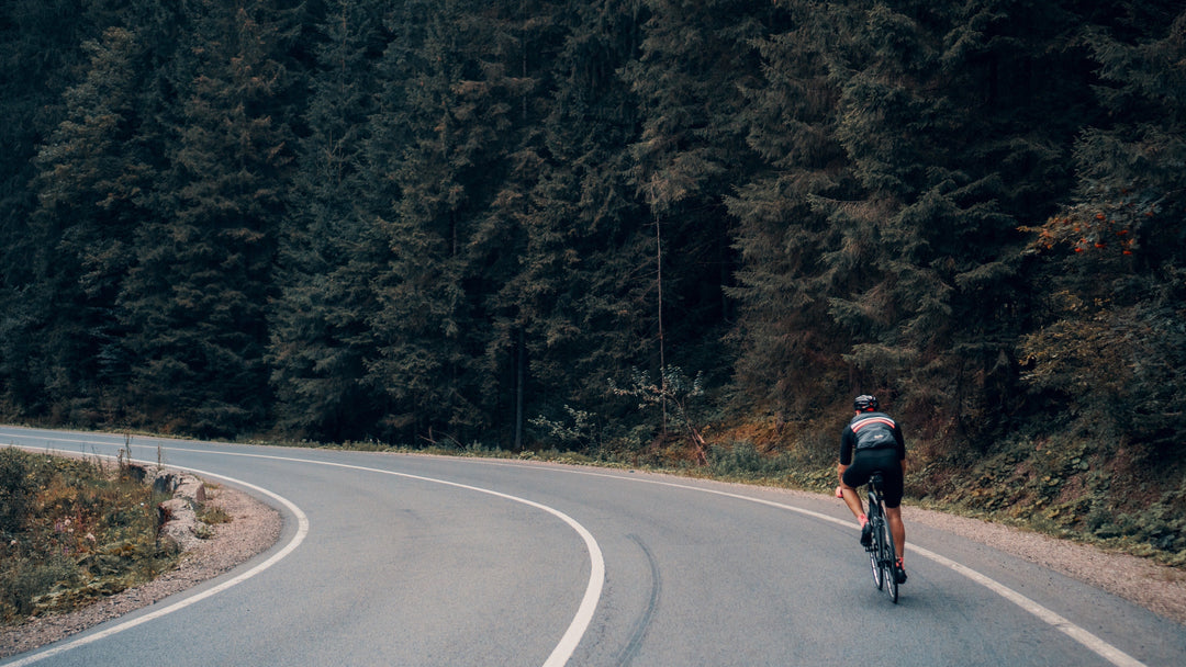 Cyclists riding road bike uphill through a forested area