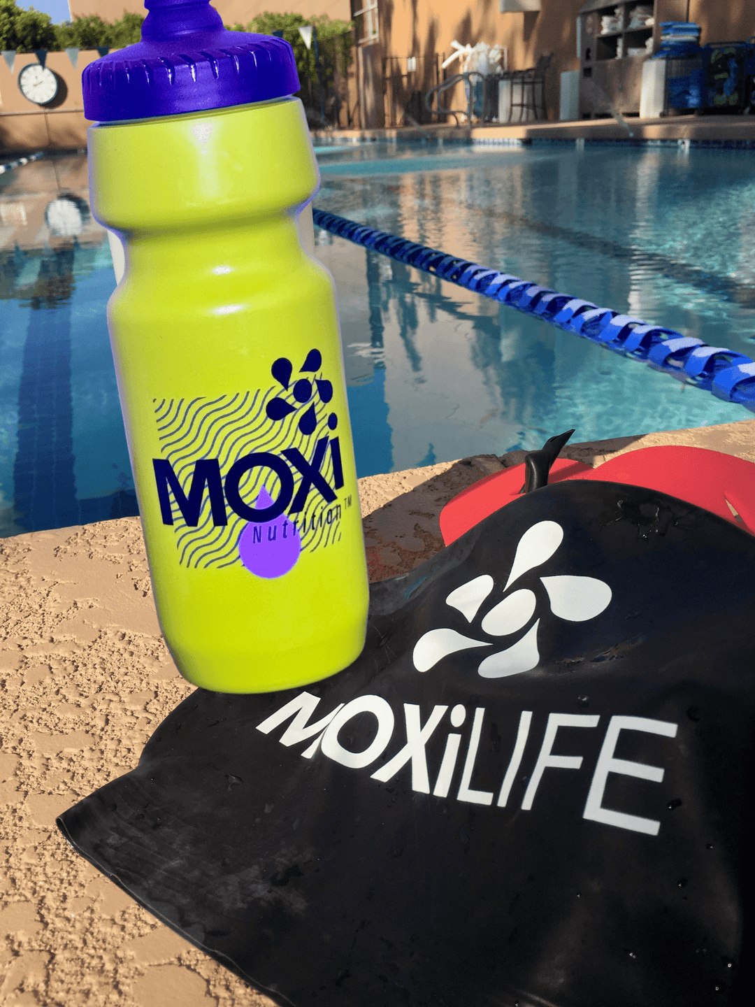 Yellow Moxi bottle with black cap on a black MoxiLife towel by a pool.